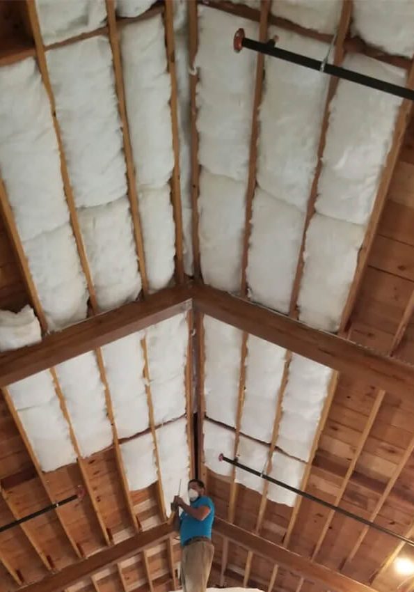 Worker installing attic insulation in exposed wooden ceiling beams